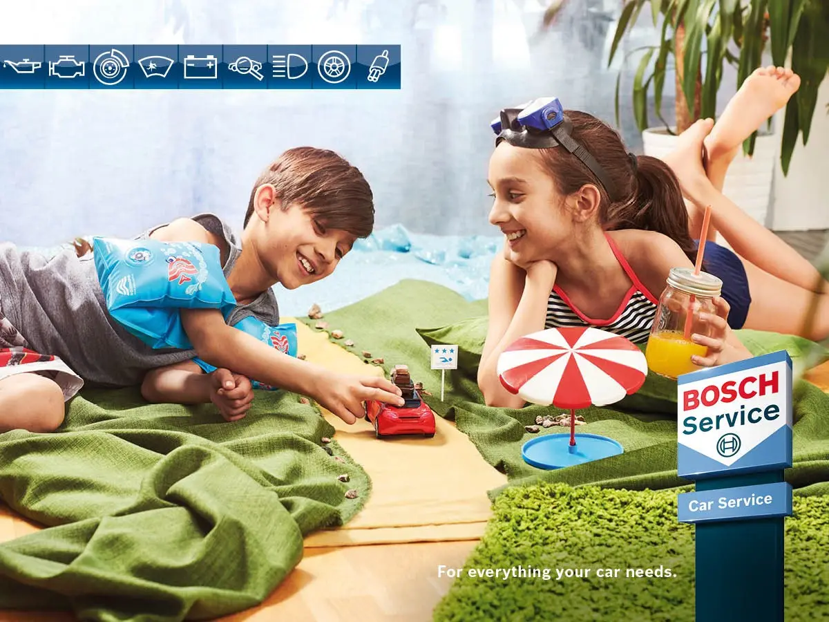 Children playing with a toy car beside a Bosch Car Service sign Alan Aston Motor Engineers
